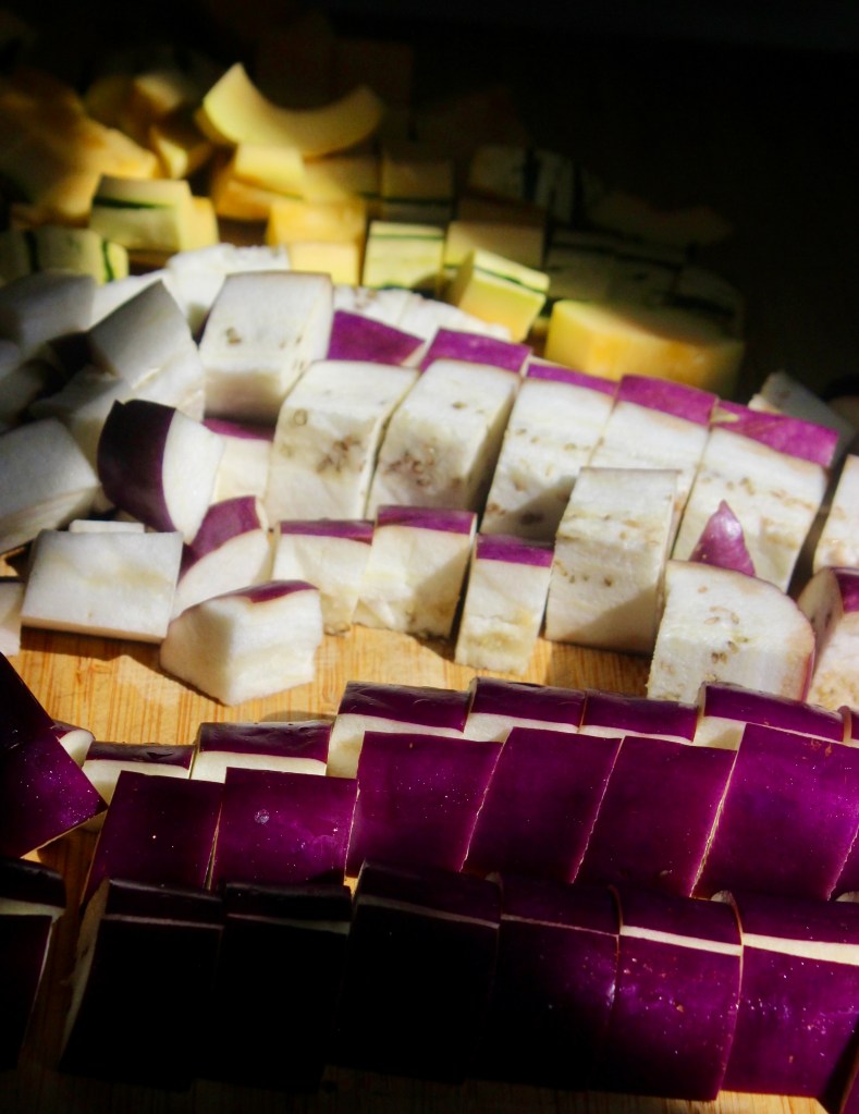 Chopped purple eggplant and other assorted vegetables on a wooden cutting board.